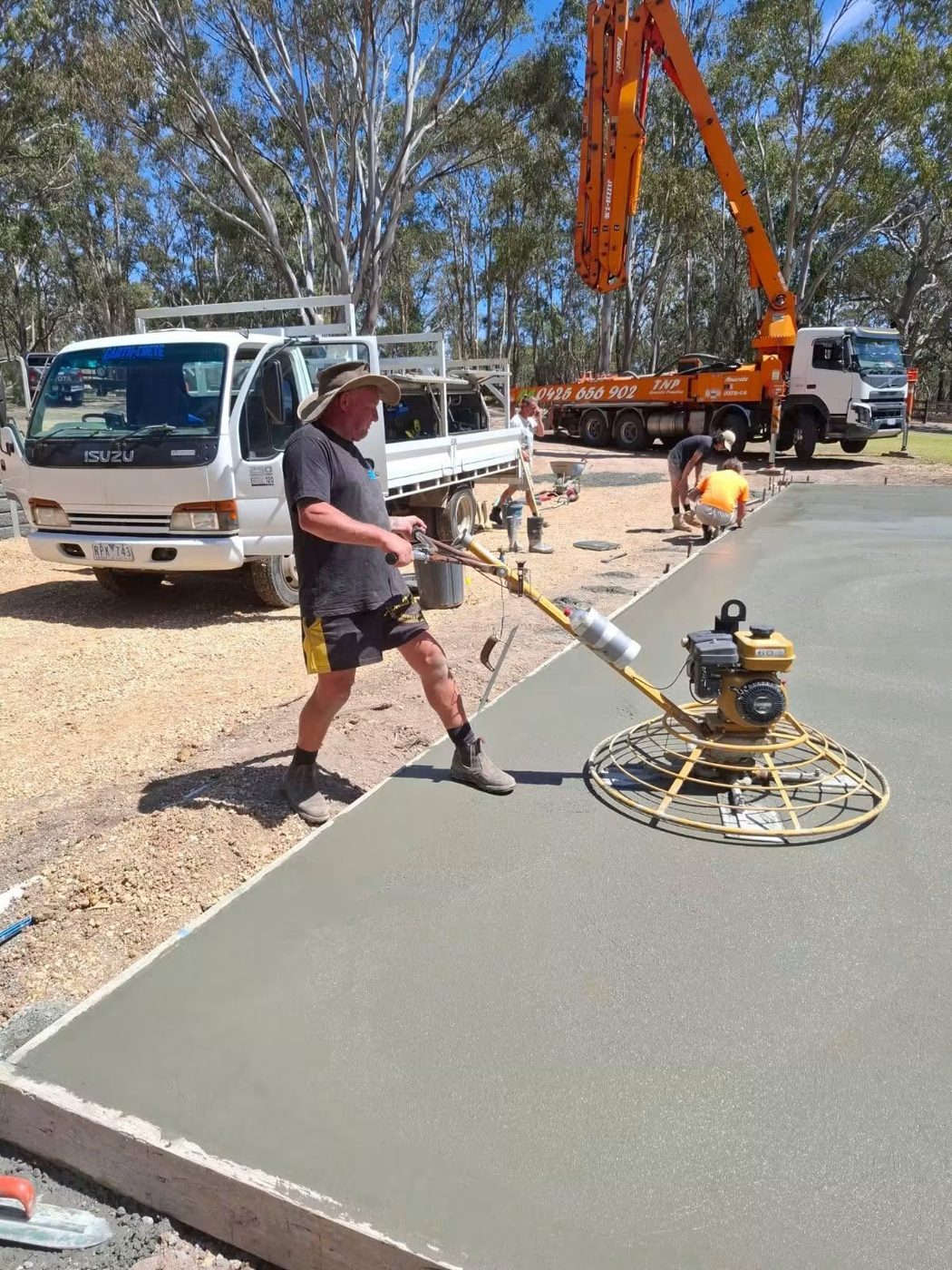 Earth-Crete crew power trowelling a large concrete slab with the Earth-Crete truck and a concrete pump behind